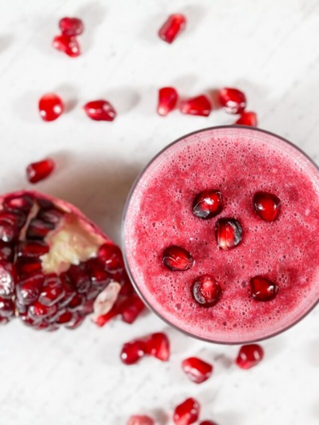 Overhead shot - glass with pomegranate smoothie, fruit berries scattered over white desk around